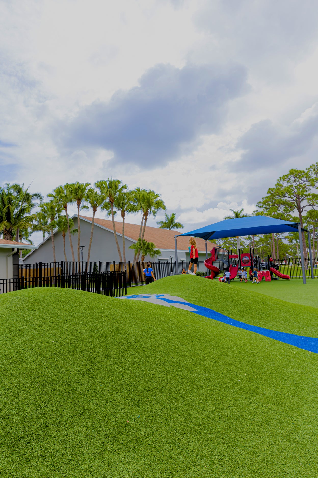 Children playing on a playground with green grass and blue sky.