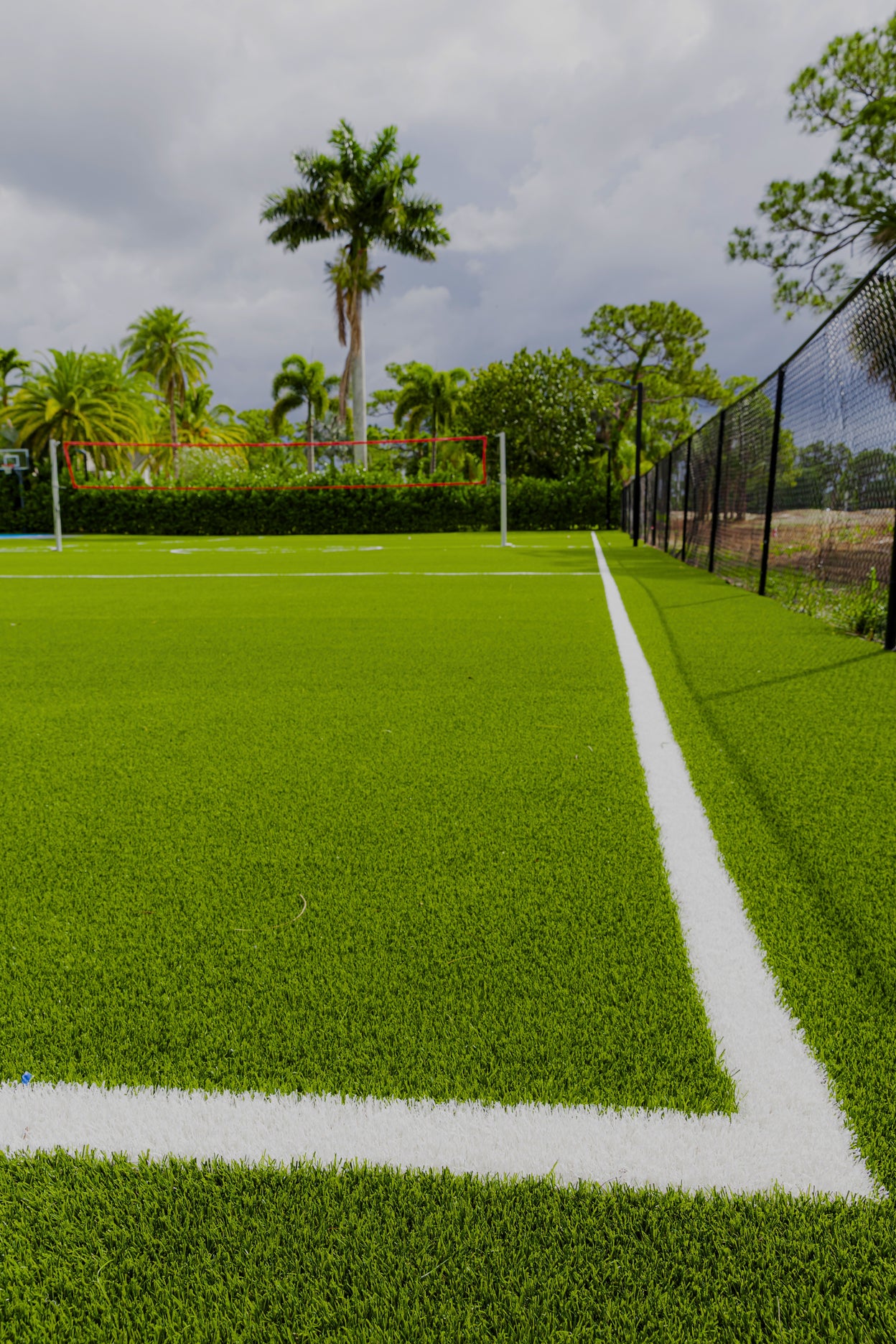 Volleyball court with net on a grassy field, surrounded by trees and a fence.