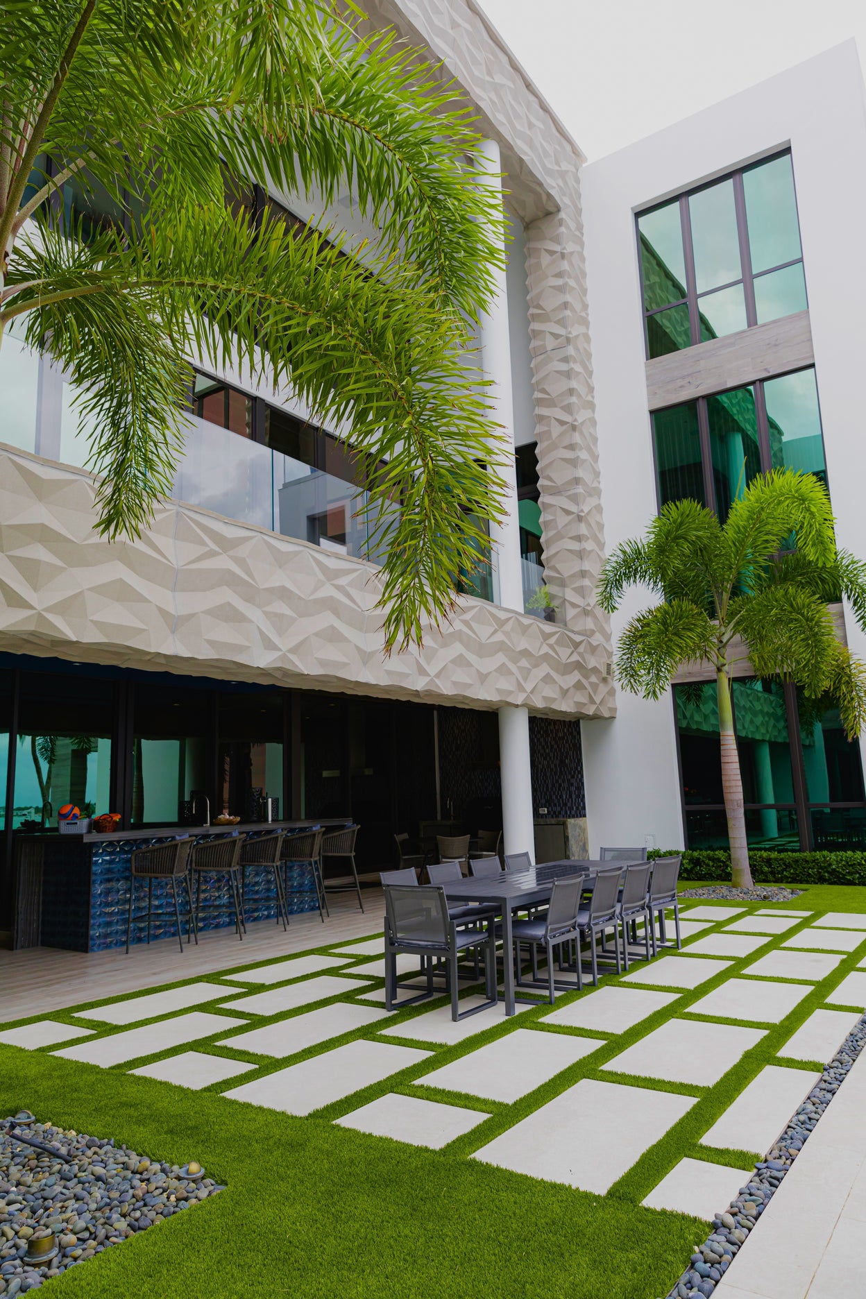 Modern outdoor patio with dining area, palm trees, and building facade.