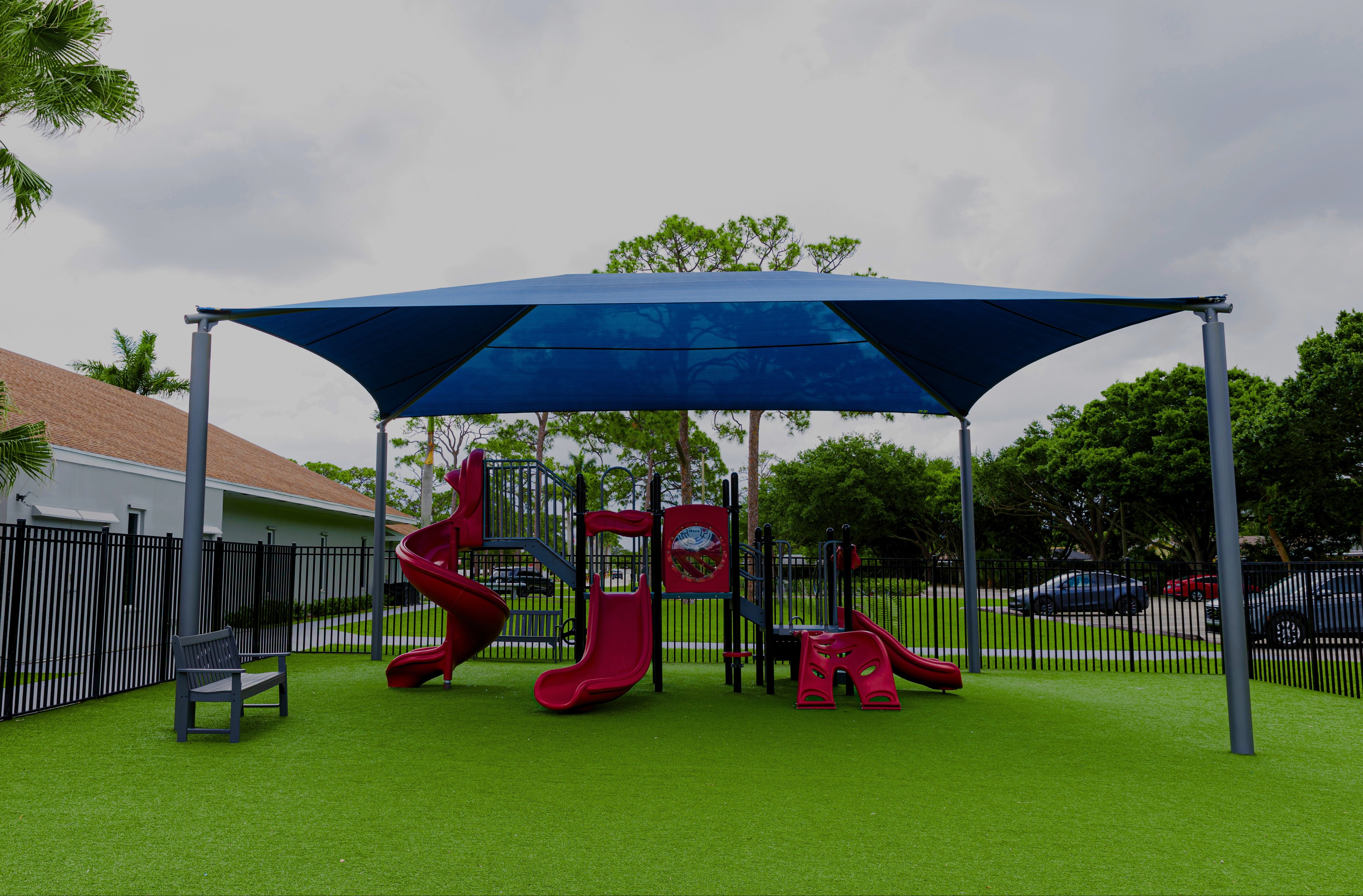 Children's playground with red slides and blue canopy under a cloudy sky.