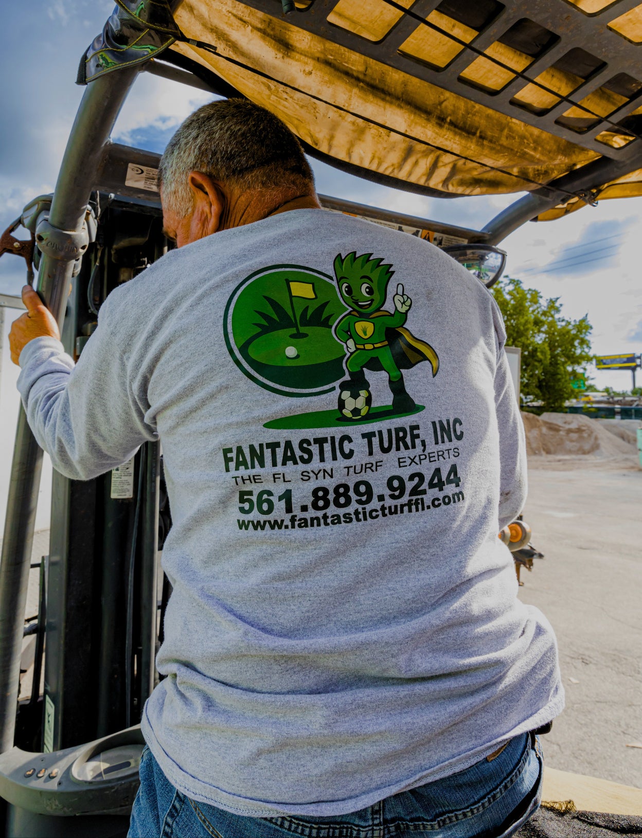 Person wearing a shirt with 'Fantastic Turf, Inc.' logo and contact information on a vehicle.