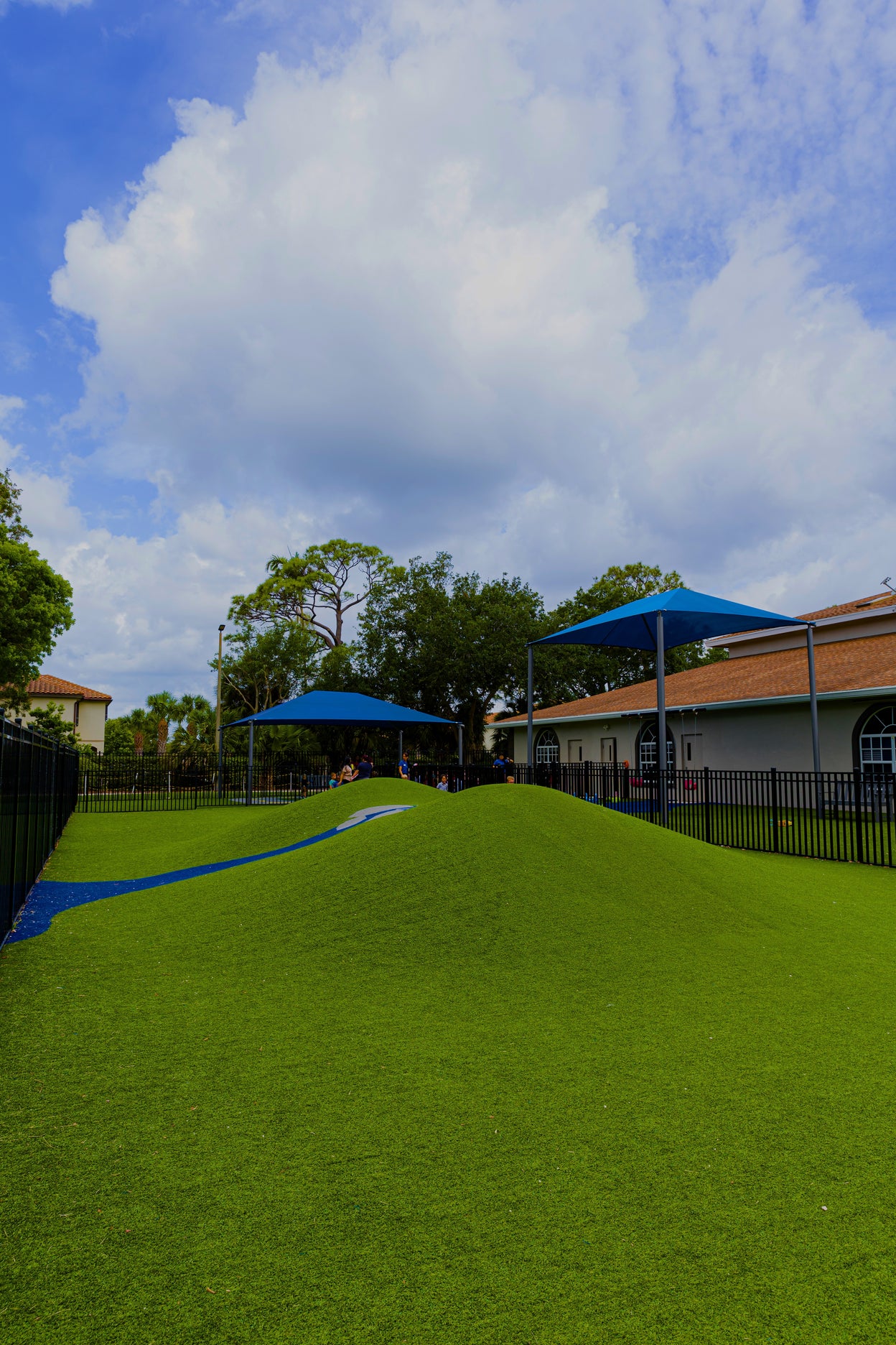 Green artificial grass field with blue canopies under a partly cloudy sky.