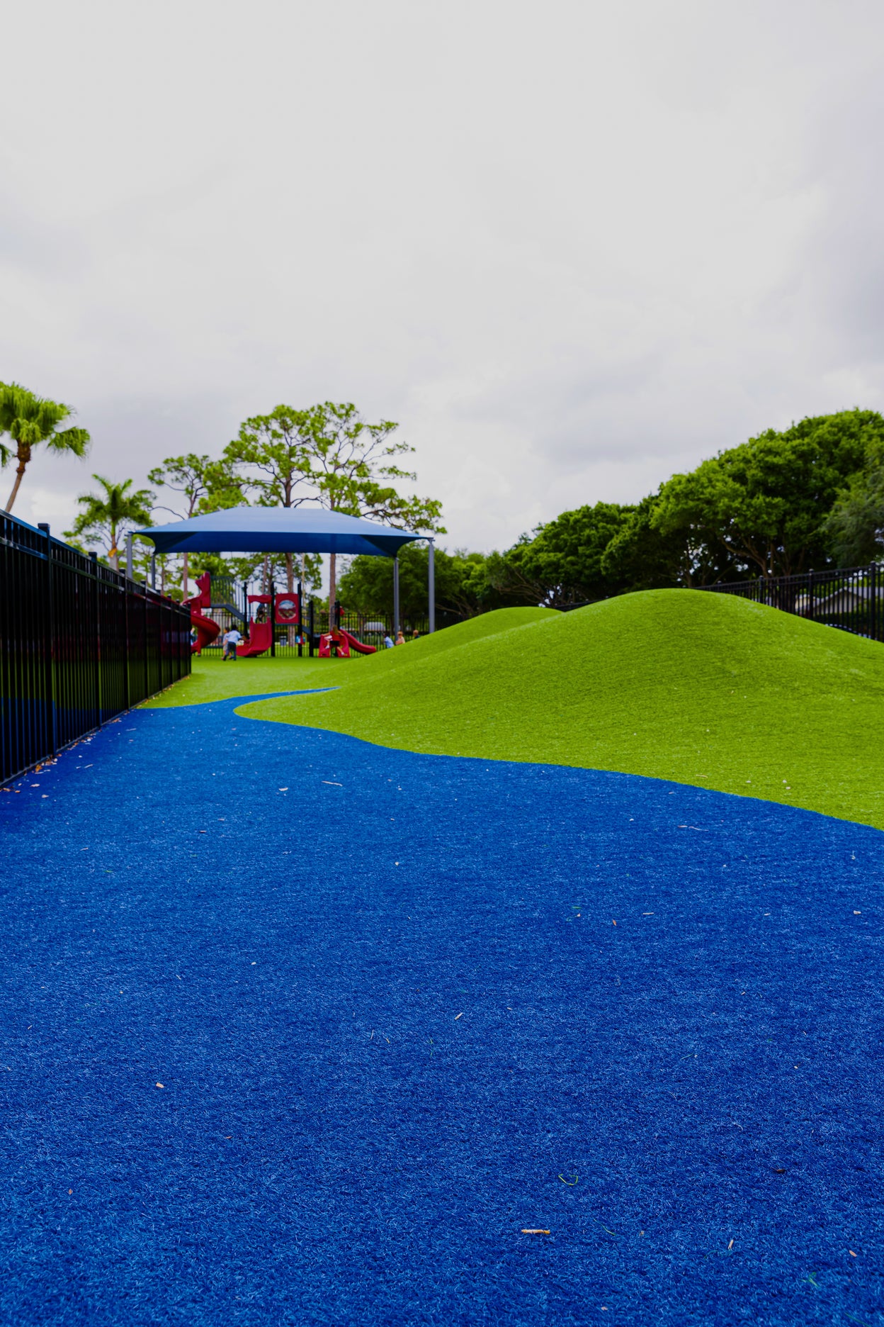 Playground with blue slide and green climbing structure against a cloudy sky.