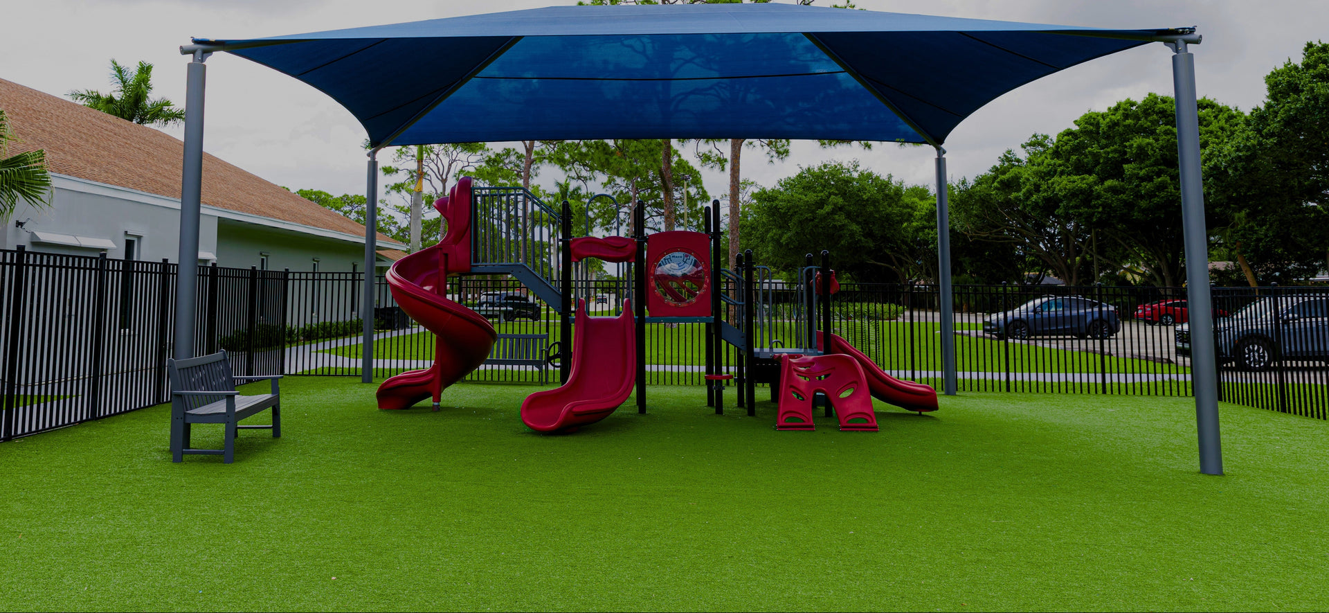 Children's playground with red slides and blue canopy under a cloudy sky.