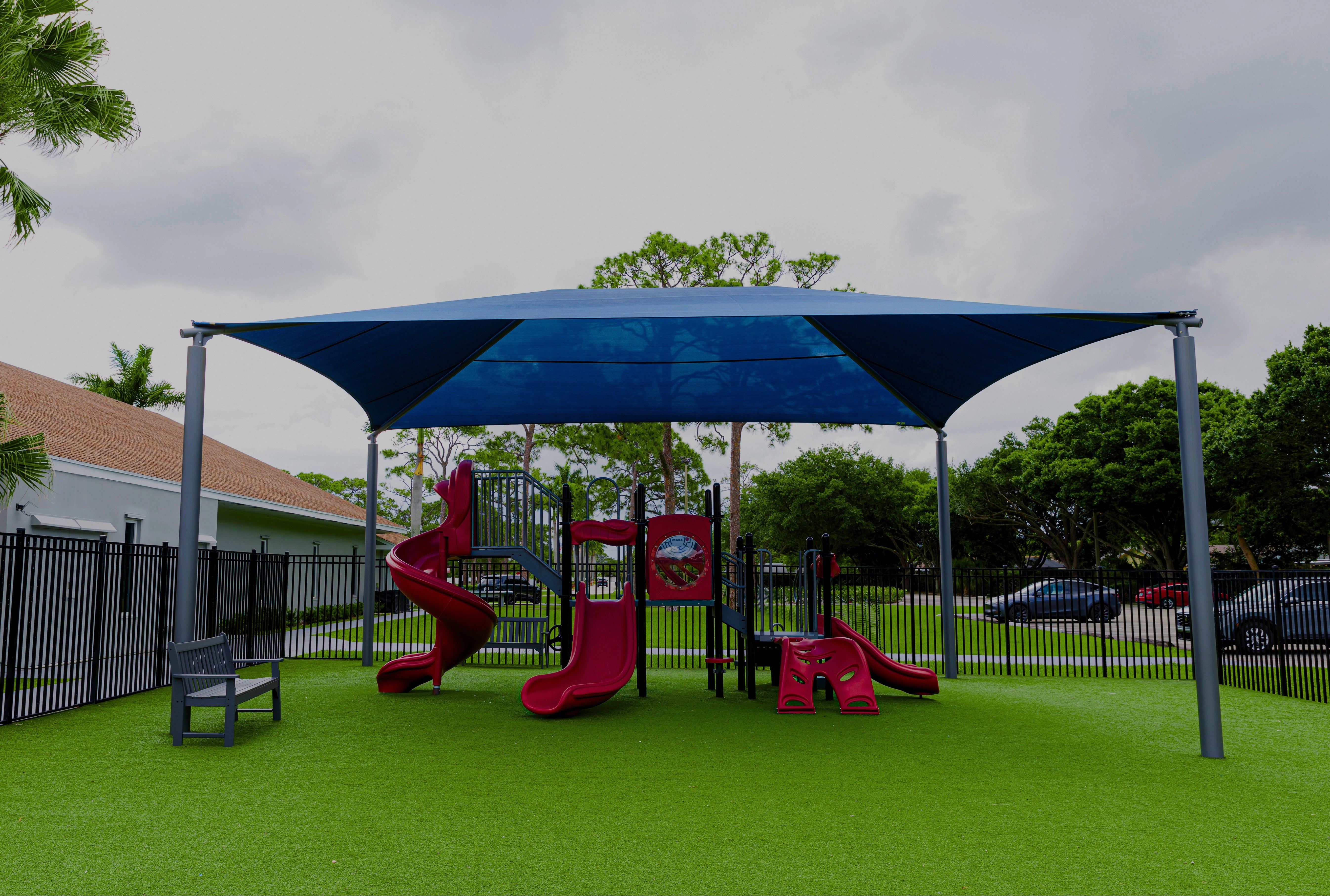 Children's playground with red slides and blue canopy under a cloudy sky.